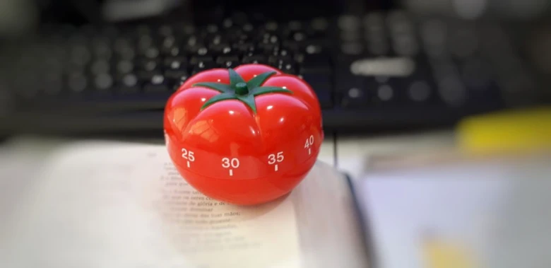 Červený pomodoro časovač ve tvaru rajčete na otevřené knize.