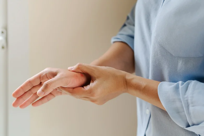 Osoba drží ruku v klíně kvůli bolesti při revmatoidní artritidě