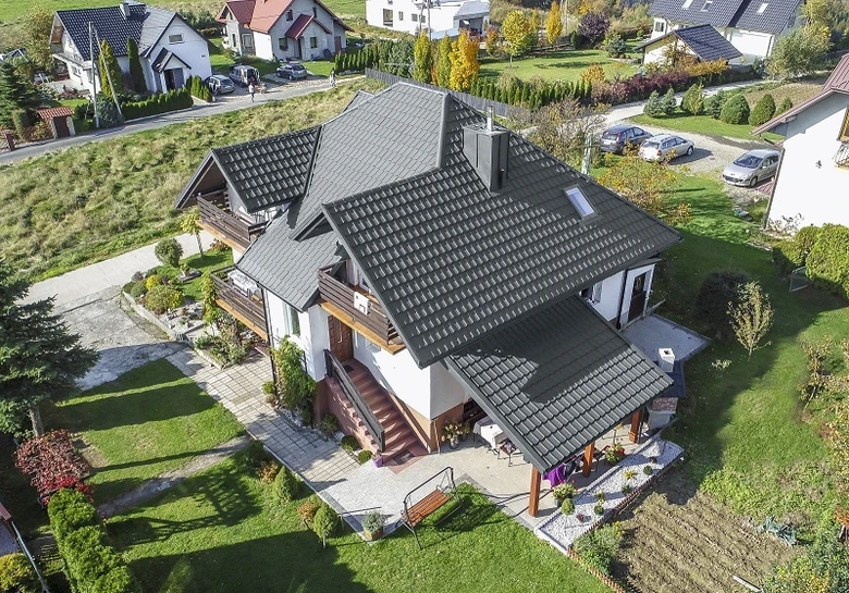 Moderní dům s tmavou sedlovou střechou na pozadí zelené zahrady.