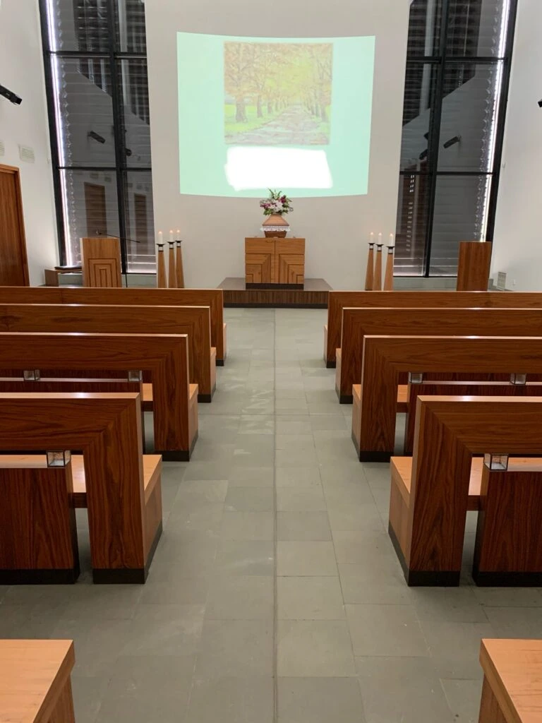 Vnitřek smuteční síně s dřevěnými lavicemi.