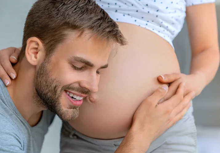 Těhotná žena s partnerem, který dotýká jejího bříška.