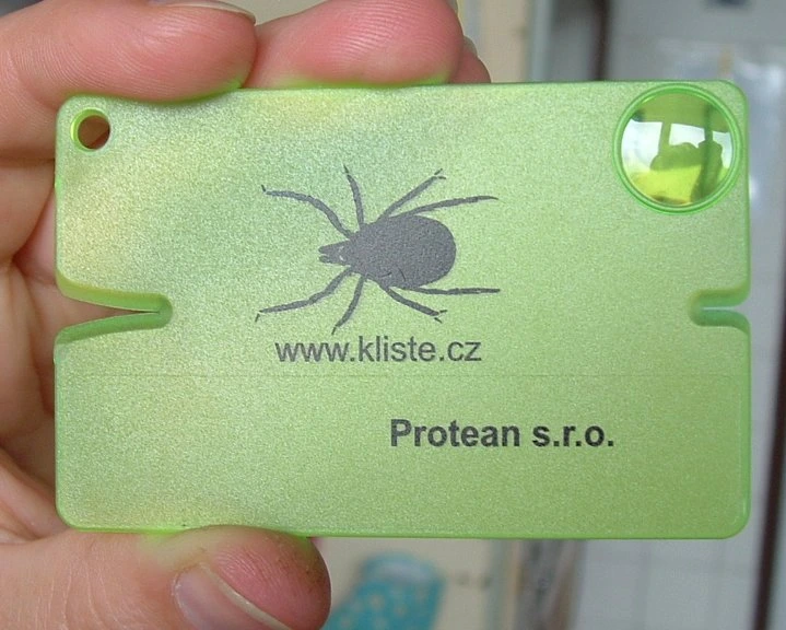 Zelený nástroj na odstranění klíště ve tvaru klíšte držený v ruce.