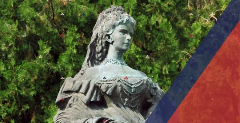Socha císařovny Sissy v historickém šatu na pozadí zelené vegetace.