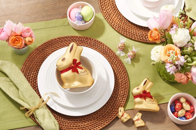 Zlatý velikonoční zajíček s čokoládami na vyzdobeném stolu.