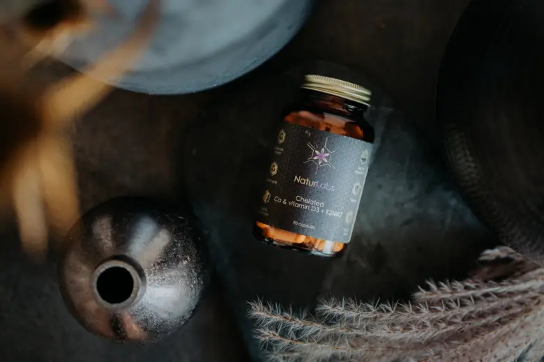 Fľaše s doplnkem vápníku, vitamínu D3 a K2 na tmavém povrchu.