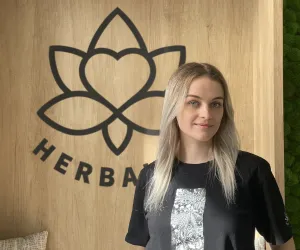 Žena stojí před dřevěnou stěnou s logem značky HerbaLife.