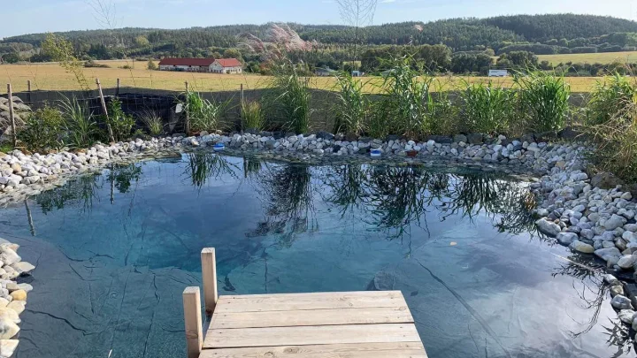 Hotový koupací jezírko s dřevěným můstkem a kameny kolem.