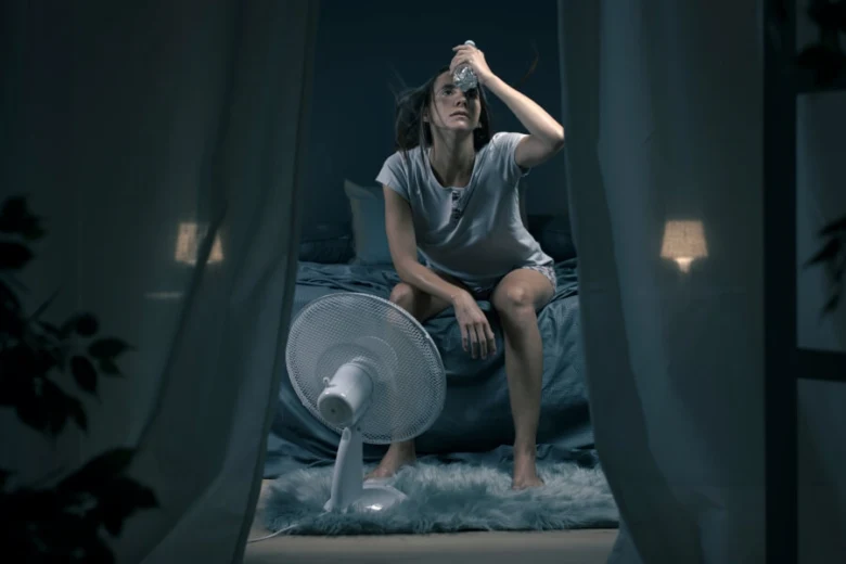 Žena v noci potí nadměrně a používá ventilátor k chlazení.