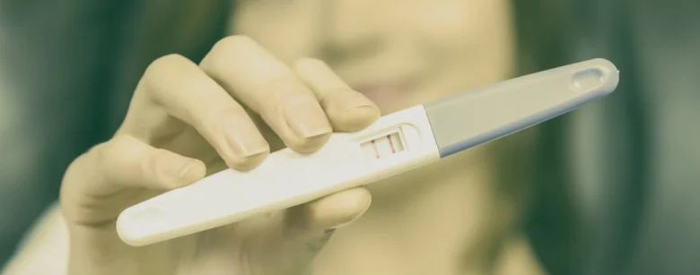 Ruka drží těhotenský test s pozitivním výsledkem dvěma čarami.