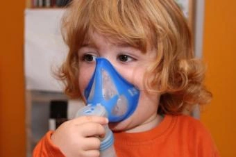 Dětský pacient používá inhalátor s modrou tvářovou maskou.