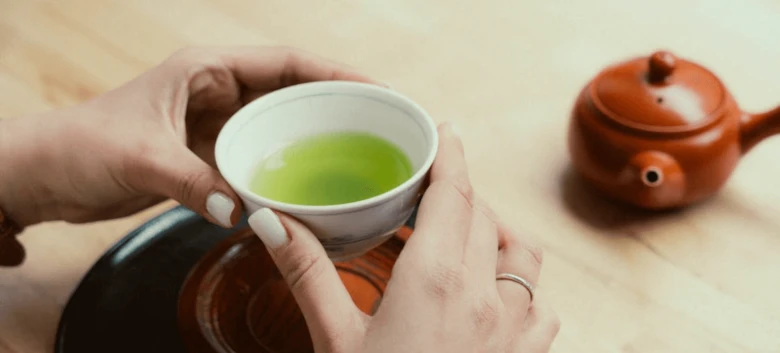 Ruce drží bílou misku s zeleným čajem matcha.