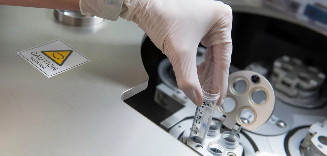 Ruka v rukavici vkládá zkumavku do laboratorního zařízení.
