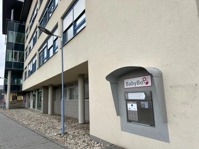 Šedý popelnicový kbelík pro výměnu dětí na fasádě budovy.