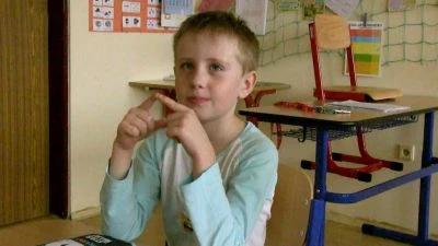Chlapec v třídě dělá gesto rukama.