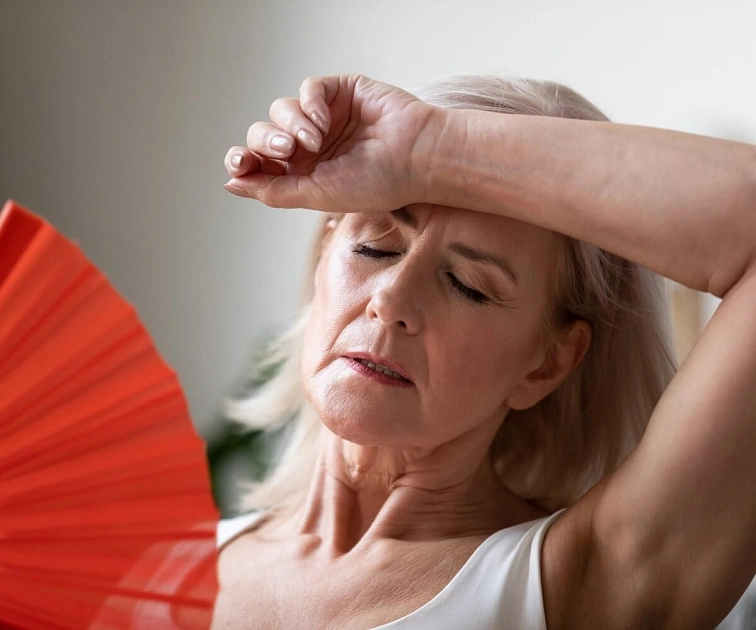 Žena s ventilátorem se snaží zvládnout horko během menopauzy.