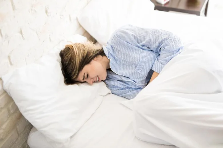 Žena leží v posteli a trpí bolestmi, typickými pro menstruační dysmenoreu.