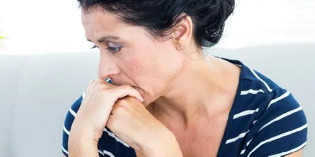 Žena sedící na gauči s rukama u úst v zoufalém stavu.