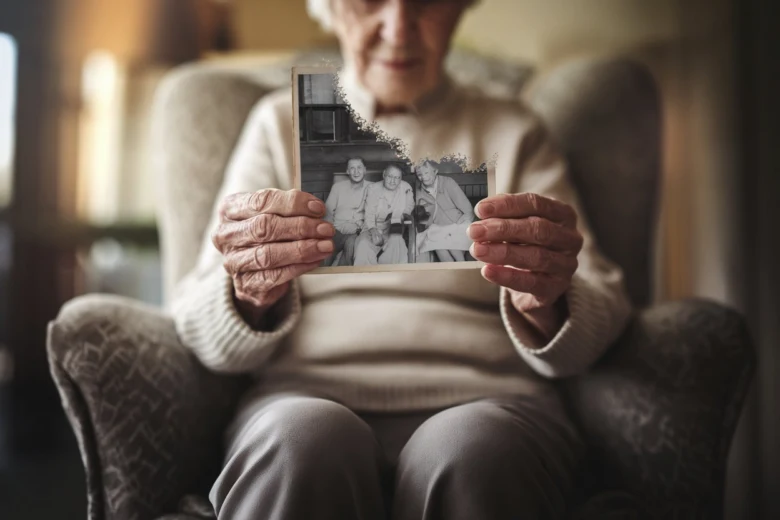 Starší žena drží starou rodinnou fotografii v křesle.