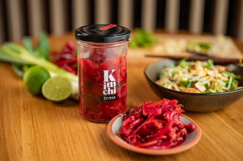 Sklenice fermentovaného kimbáče s čerstvými ingrediencemi na dřevěném stole.