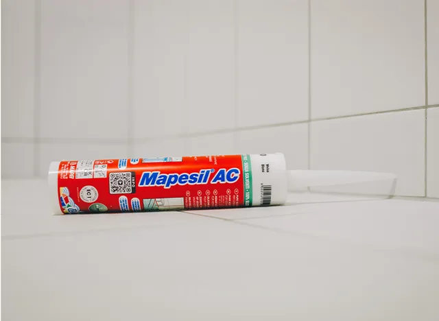 Tubka silikonu na dlažbě v koupelně pro těsnění.