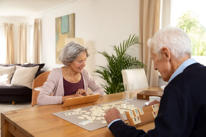 Dvojice seniorů hraje společně na stole v obývacím pokoji.