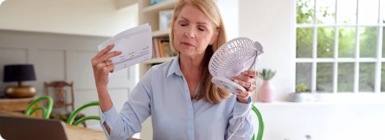 Žena drží papíry a malý ventilátor v interiéru.