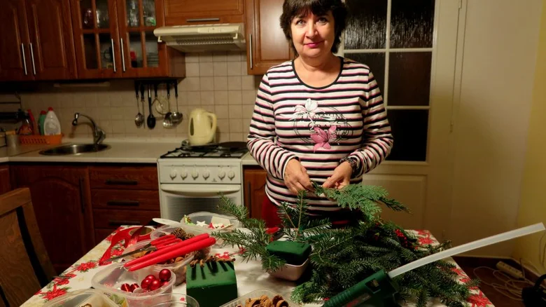 Žena v kuchyni tvoří vánoční svícen z větví jehličnanu.