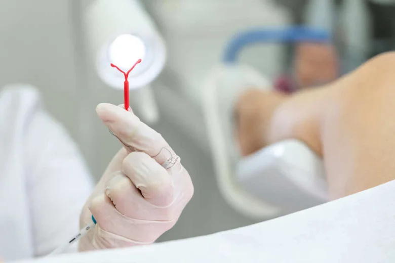 Rukou v rukavicích je drženo červené nitroděložní tělísko před vložením.