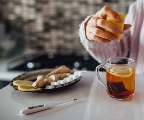 Člověk stlačí citron do čaje s ingvem vedle teploměru.