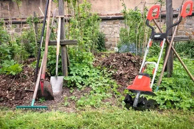 Červený rotavátor mezi zahradními nářadími v zelené zahrádce