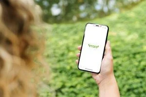 Ruka drží chytrý telefon venku před zelenou přírodou.