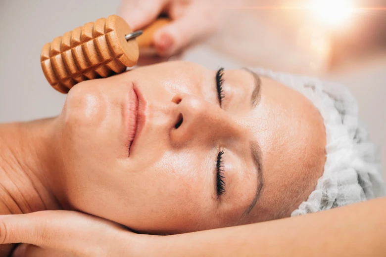 Žena relaxuje při masáži obličeje dřevěným válečkem.