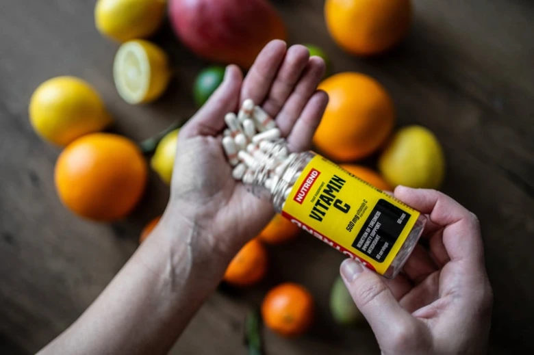 Ruce s tabletami vitamínu C mezi citrusovými plody na dřevěném povrchu.