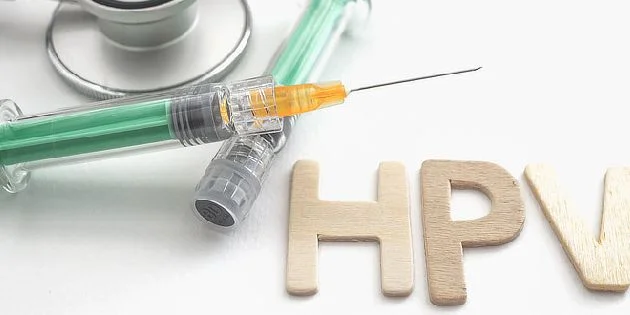 Střiková jehla, fonendoskop a dřevěné písmena HPV na bílém pozadí.