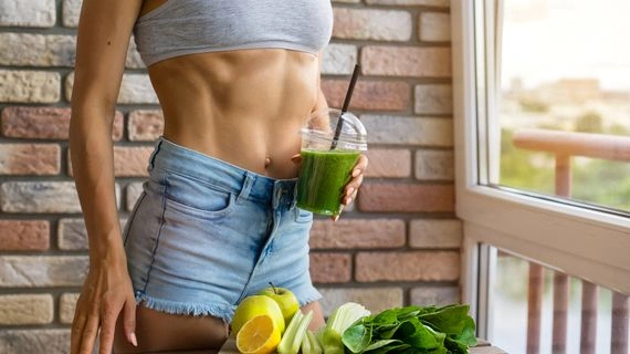Žena s zeleným smoothiem a čerstvou zeleninou u okna.