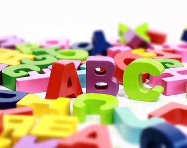 Rozptýlené barevné plastové písmena ABC na bílém pozadí.