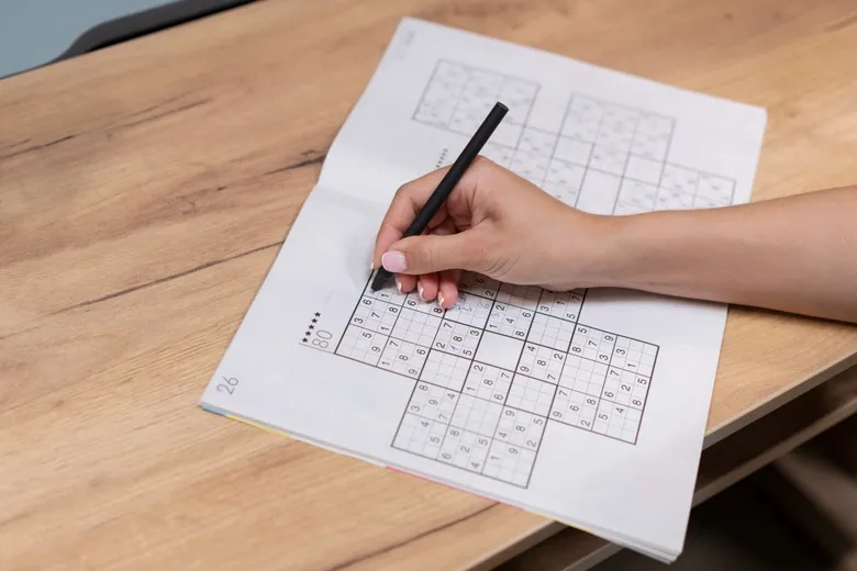 Ruka píše čísla do sudoku na papíře pro trénit mozek