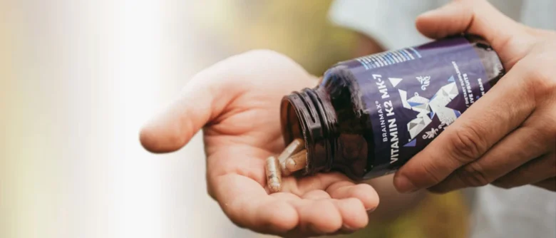 Ruce s lahvičkou vitamínu K2 MK-7, kapsule v dlani.