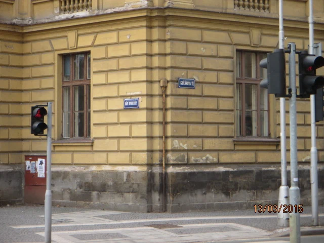 Modlé tabule s číslem popisným a názvem ulice na žlutém domě.