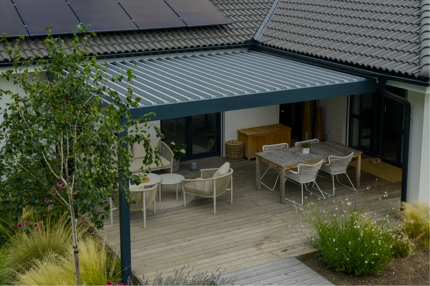 Moderní pergola s dřevěnou terasou, sedacími místy a zahradním nábytkem.