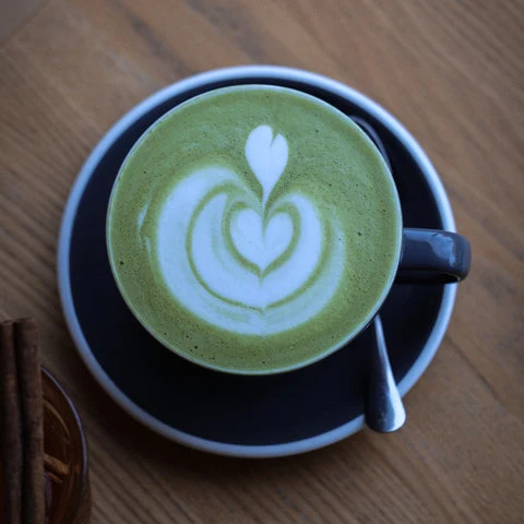Černá šálka s matcha lattes na podšálku se srdcem z pěny.