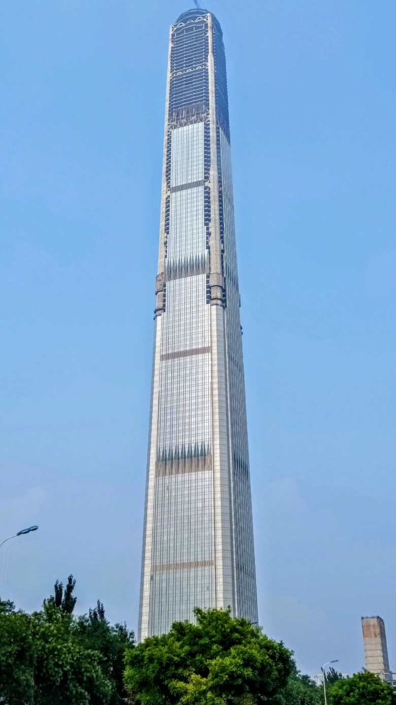 Shanghai Tower ve výstavbě na modré obloze s stromy dole.