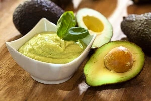 Mísa s guacamolem vedle polovičního avokáda na dřevěném povrchu.