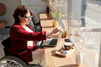 Žena v invalidním vozíku pracuje u počítače při denním světle.