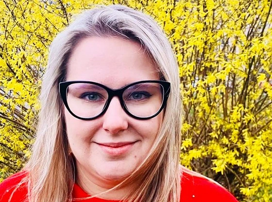 Žena v brýlích s červeným tričkem před žlutými květy.