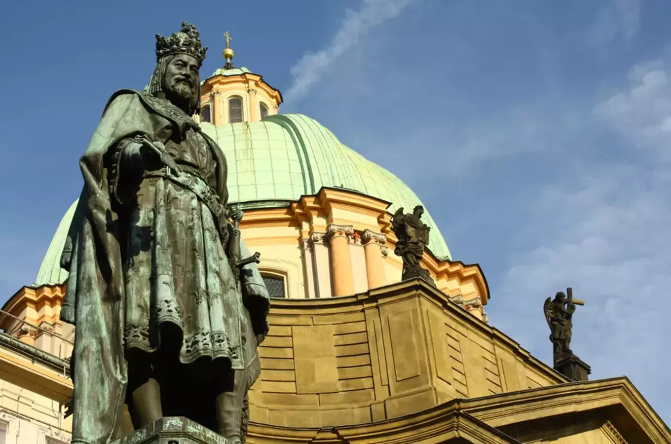 Socha Karla IV před kostelem s kupolí na modré obloze.