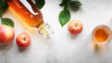 Sklenička jablkového octu s jablky a listy na světlém pozadí.