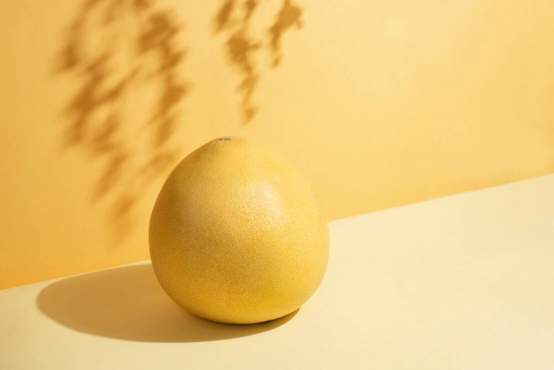 Žlutý pomelo na světlém povrchu s stínem listů.