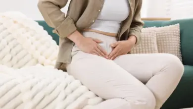 Žena sedí na gauči a drží si bolavé břicho.