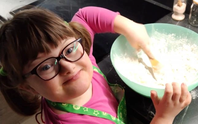 Dívka s Downovým syndromem míchá těsto v misce.